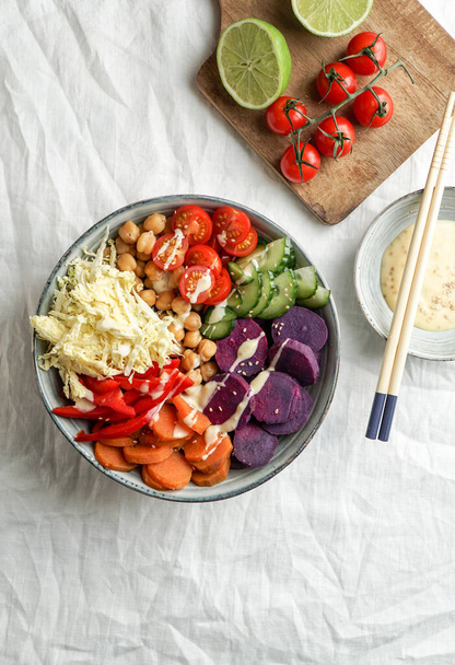 budha bowl with purple batata, bell peppers, cabbage, sweet potatoes, chickpeas, cucumbers on the white linen tablecloth - Photo, Image