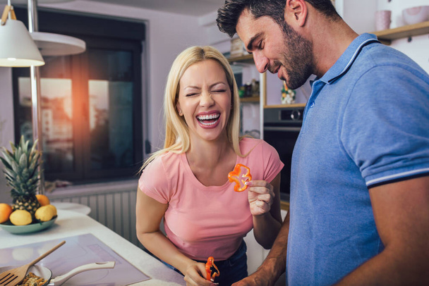 Casal jovem sorrindo enquanto cozinha comida saudável na cozinha em casa. - Foto, Imagem