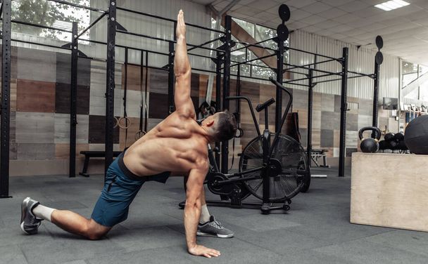 Junger muskulöser Mann übt Muskeldehnung in modernem Fitnessstudio - Foto, Bild