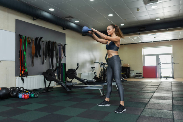 Mujer musculosa joven en ropa deportiva entrena kettlebell swing en el gimnasio. Concepto de estilo de vida saludable. Entrenamiento funcional - Foto, Imagen