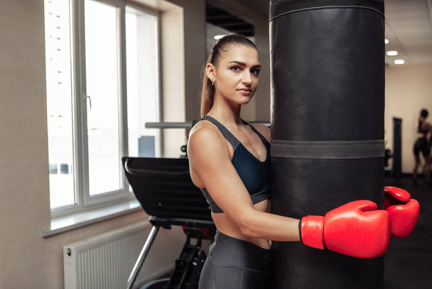 Kobieta bokser, zmęczony po intensywnym treningu, przytula worek bokserski - Zdjęcie, obraz