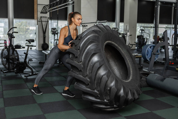 Young cross fit woman pushing heavy big wheel in modern gym. Functional training. Healthy lifestyle - Fotó, kép