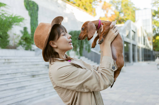 Retrato de una joven mujer de moda y un encantador cachorro salchicha en un parque de la ciudad. Amante y mascota - Foto, imagen