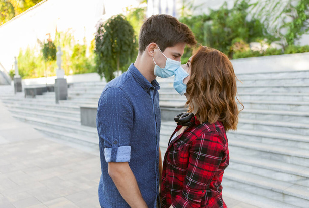 Young Couple in love, man and woman kissing each other in protective medical mask on face outdiir. Environmental pollution concept. Pandemic coronavirus( covid-19), virus protection - Photo, Image