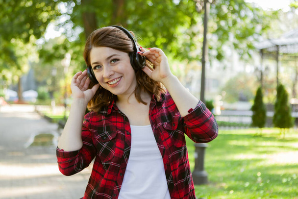 Nuori iloinen hauska nainen kuuntelee musiikkia kuulokkeilla kaupungin puistossa - Valokuva, kuva