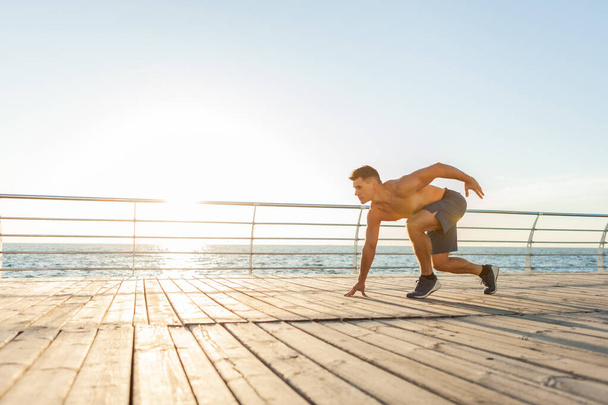 Uomo muscoloso con busto nudo pronto a correre all'alba sulla spiaggia - Foto, immagini