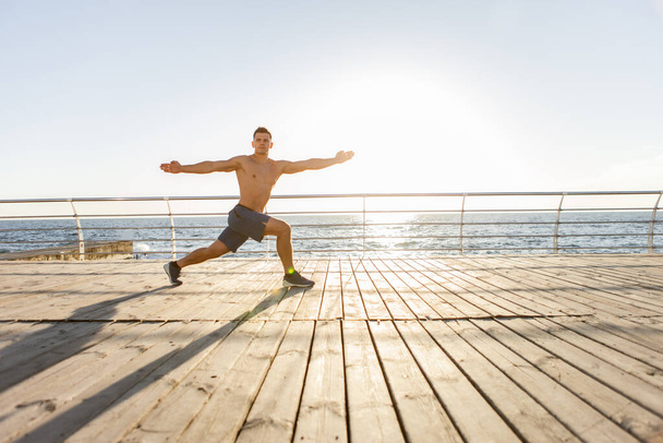 Mladý svalnatý muž cvičí jógu asana při východu slunce na pláži - Fotografie, Obrázek