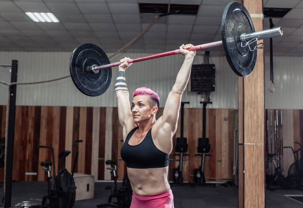Potężny i silny kulturysta kobieta robi nad głową z ciężkimi sztangi w nowoczesnym cross siłowni. Trening funkcjonalny. Kulturystyka i fitness - Zdjęcie, obraz