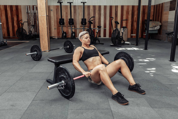 Mujer fuerte atlética joven practicando ejercicio de puente de glute con una pesada barra en las piernas. Culturismo y Fitness - Foto, Imagen