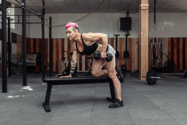 Спортсменка виконує вправи з гантелі одним рухом. Тренування м'язів спини. Бодібілдінг та фітнес
 - Фото, зображення