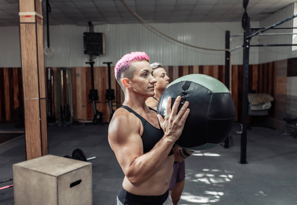 Muskularne atletyczne kobiety trenują z kulkami lekarskimi w nowoczesnej siłowni. Cross fit, trening funkcjonalny - Zdjęcie, obraz
