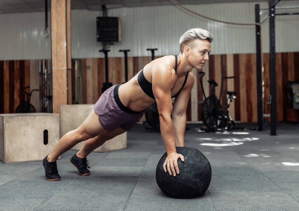 Musculosa mujer atlética flexiones con bolas de medicina en un gimnasio moderno. Crossfit, entrenamiento funcional - Foto, Imagen