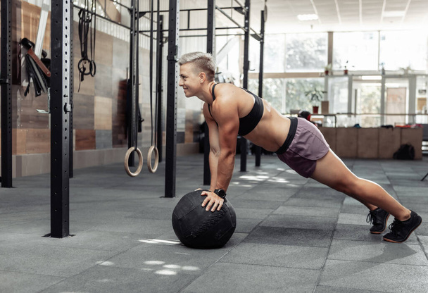 Muskularna atletyczna kobieta pompuje piłki medyczne w nowoczesnej siłowni. Cross fit, trening funkcjonalny - Zdjęcie, obraz