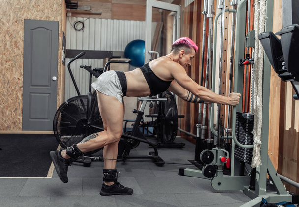 Мышечное бодибилдинг женщина тренирует мышцы бедра в кроссовер кабельной машине. Фитнес-концепция - Фото, изображение