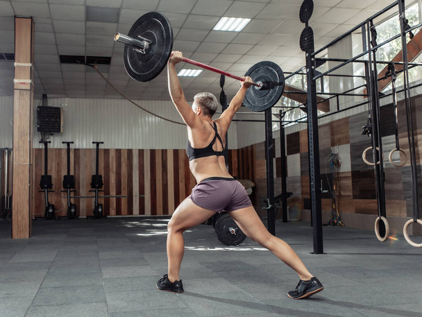 Erős és erős női testépítő csinál fölött nehéz súlyzó a modern cross tornaterem. Funkcionális képzés. Testfelépítés és alkalmasság - Fotó, kép