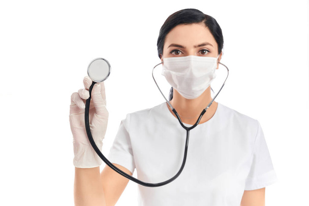 Qualified doctor in medical protective mask using stethoscope - Foto, afbeelding