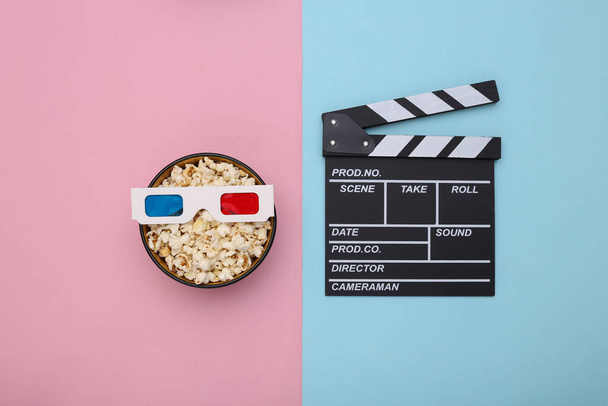 Popcorn bowl with 3d glasses, clapperboard on pink blue pastel background. Movie time - Photo, Image