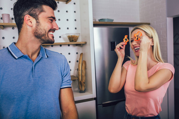 Young couple smiling while cooking healthy food in kitchen at home. - Photo, Image