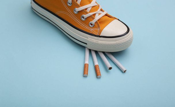 Gumshoe sapatilha pisou cigarros em um fundo azul. Deixar de fumar conceito - Foto, Imagem