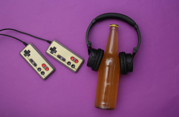 Eğlence zamanı. Oyun pedleri ve mor arka planda kulaklıkları olan bira şişesi. Üst görünüm - Fotoğraf, Görsel