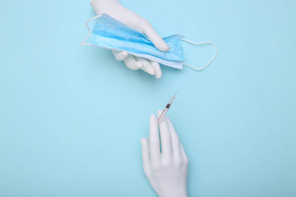 Mannequin Hände halten medizinische Maske und Spritze auf blauem Hintergrund. Medizinkonzept - Foto, Bild