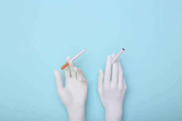 White mannequin hands hold  cigarettes on blue background. Smoking addiction - 写真・画像