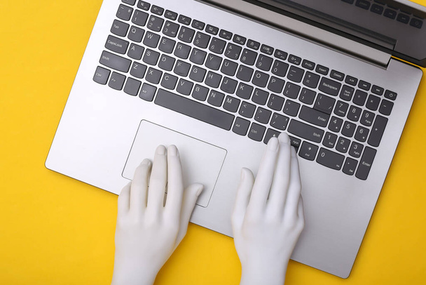 Mannequin handen zijn typen op laptop toetsenbord en het houden van sigaret op gele achtergrond. Bovenaanzicht - Foto, afbeelding