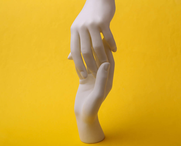 Белые руки манекена касаются друг друга на желтом фоне. Минимализм. Концепт-арт - Фото, изображение