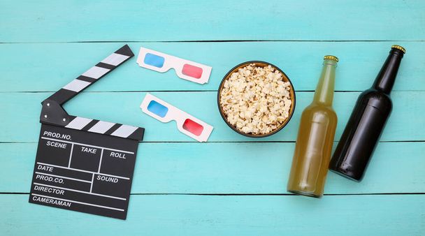 E 'l'ora del cinema. Bordo del film, bicchieri 3d, bottiglie di birra, popcorn su sfondo blu di legno. Vista dall'alto - Foto, immagini