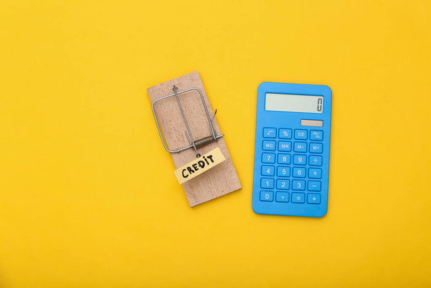 Pułapka na myszy z przynętą i kalkulatorem na żółtym tle. Pojęcie pułapki, ryzyka lub oszustwa - Zdjęcie, obraz