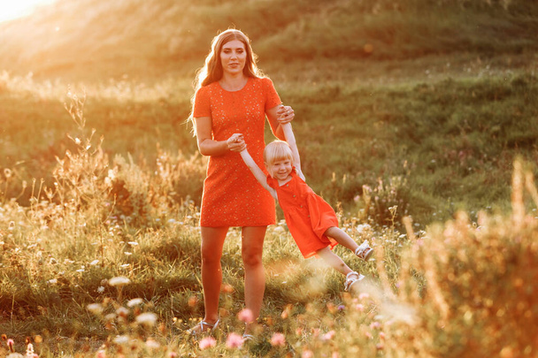 Portrait of a mother holds, throws up and spins the daughter on hands on nature on summer day vacation. Mom and girl playing in the park at the sunset time. Concept of friendly family. Close Up. - Photo, Image