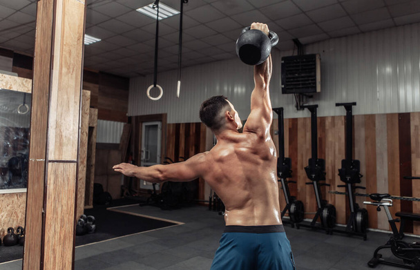Güçlü kaslı bir adam spor salonunda ağır bir kettlebell ile egzersiz yapıyor. Serbest ağırlık ile fonksiyonel eğitim - Fotoğraf, Görsel