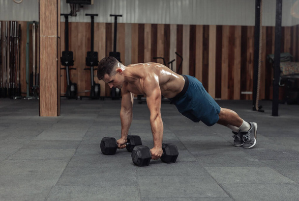 Muscular powerful man doing push-ups with dumbbells in gym - Photo, image