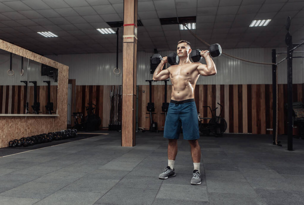 Ισχυρός αθλητικός άνθρωπος προπόνηση μυών ώμου με βαριά αλτήρες στο γυμναστήριο - Φωτογραφία, εικόνα
