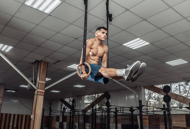Gespierde mannelijke turnster die in een moderne fitnessclub op gymnastiekringen traint. Gezond levensstijl concept - Foto, afbeelding