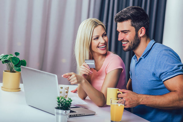 Happy couple at home paying bills with laptop and credit card - Photo, Image