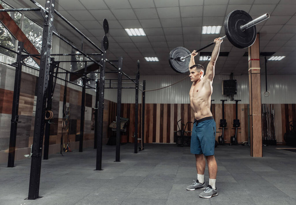Izmos ember gyakorolja a nehéz súlyzót a modern fitneszklubban. Testfelépítés és alkalmasság - Fotó, kép