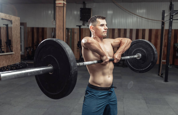 Спортивный мускулистый человек, тренирующийся с тяжелой штангой в современном оздоровительном клубе. Культуризм и фитнес - Фото, изображение