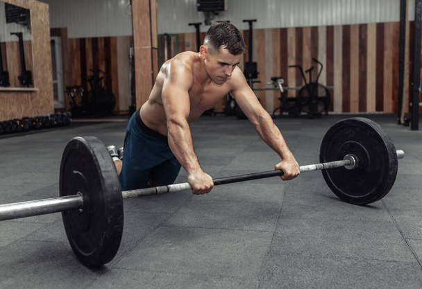 Αθλητικός μυώδης άνδρας που γυμνάζεται με βαρελάκι στο σύγχρονο γυμναστήριο. Bodybuilding και Γυμναστήριο - Φωτογραφία, εικόνα
