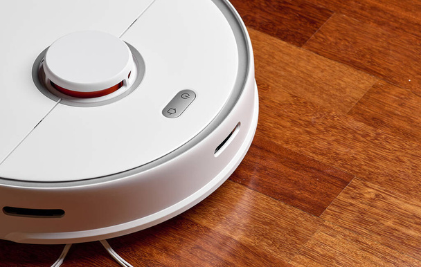 Smart Robot Vacuum Cleaner on wood floor. Robot vacuum cleaner performs automatic cleaning of the apartment at a certain time. Smart home - Foto, Bild