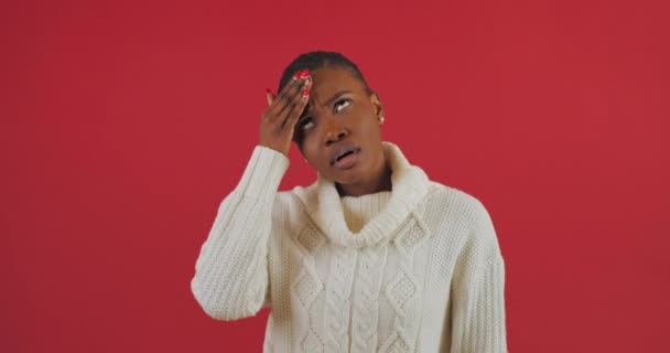 Портрет африканської жінки, яка тримає голову від головного болю, напружений смуток через проблеми на роботі, ізольований на червоному тлі, сумний вираз обличчя жінки. - Кадри, відео