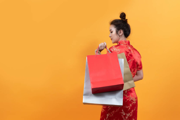 Красивая девушка Азии носить Cheongsam держать торговые сумки в китайском новом году на желтом фоне. - Фото, изображение