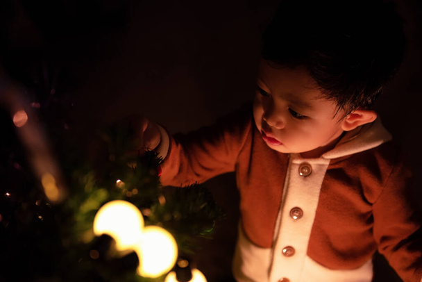 家の中で夜にクリスマスツリーを飾る小さな男の子 - 写真・画像