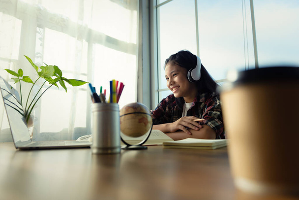 Asiatische junge Frauen oder Studentinnen, die am Tisch sitzen, entspannen sich mit ihren Kopfhörern, während sie nach dem Lernen zu Hause auf ihren Laptop schauen. Stressabbau, erfolgreiche gute Ergebnisse, Bildung von zu Hause aus. - Foto, Bild
