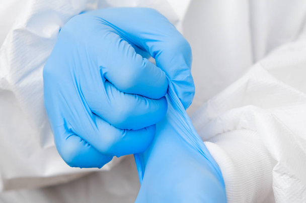Doctor or nurse in protective PPE suit putting on rubber blue gloves before work with coronavirus patient or test samples or vaccination - Foto, immagini