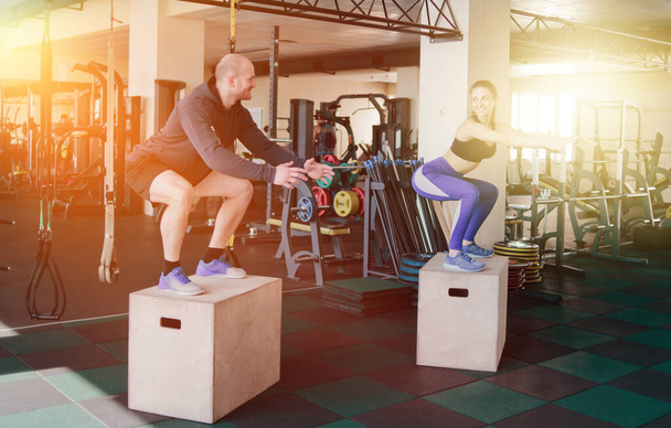 Couple functional training. Fitness man and woman jump on the wooden boxes in the gym - Photo, Image