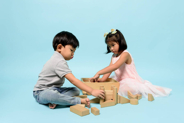 Asyalı iki çocuk, stüdyodaki pastel mavisi arka planda tahta oyuncaklarla eğlenmek için birlikte oynuyorlar. Çocukların becerileri, çocukluk rolleri ve doğum düzeni, çocuk gelişimi kavramı. - Fotoğraf, Görsel