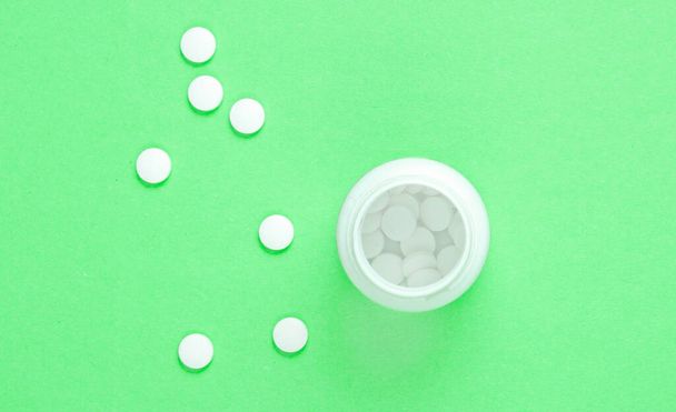 Minimalistic medical concept. Open bottle with white pills on green pastel background. Top view - Fotografie, Obrázek