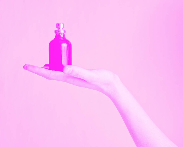 Female hand holding bottle of perfume on the palm with pink toned - 写真・画像
