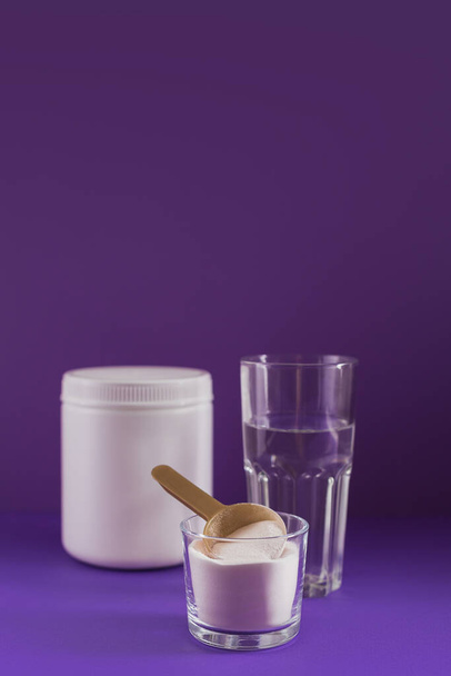 Collagen powder in bowl, glass of water and measure spoon on purple background. Extra protein intake. Natural beauty and health supplement concept. - Фото, зображення